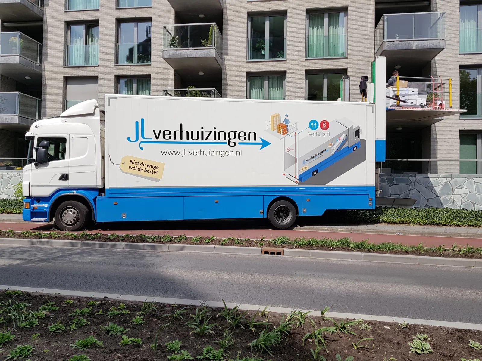 Verhuiswagen bij een appartementencomplex, verhuislift aan het balkon